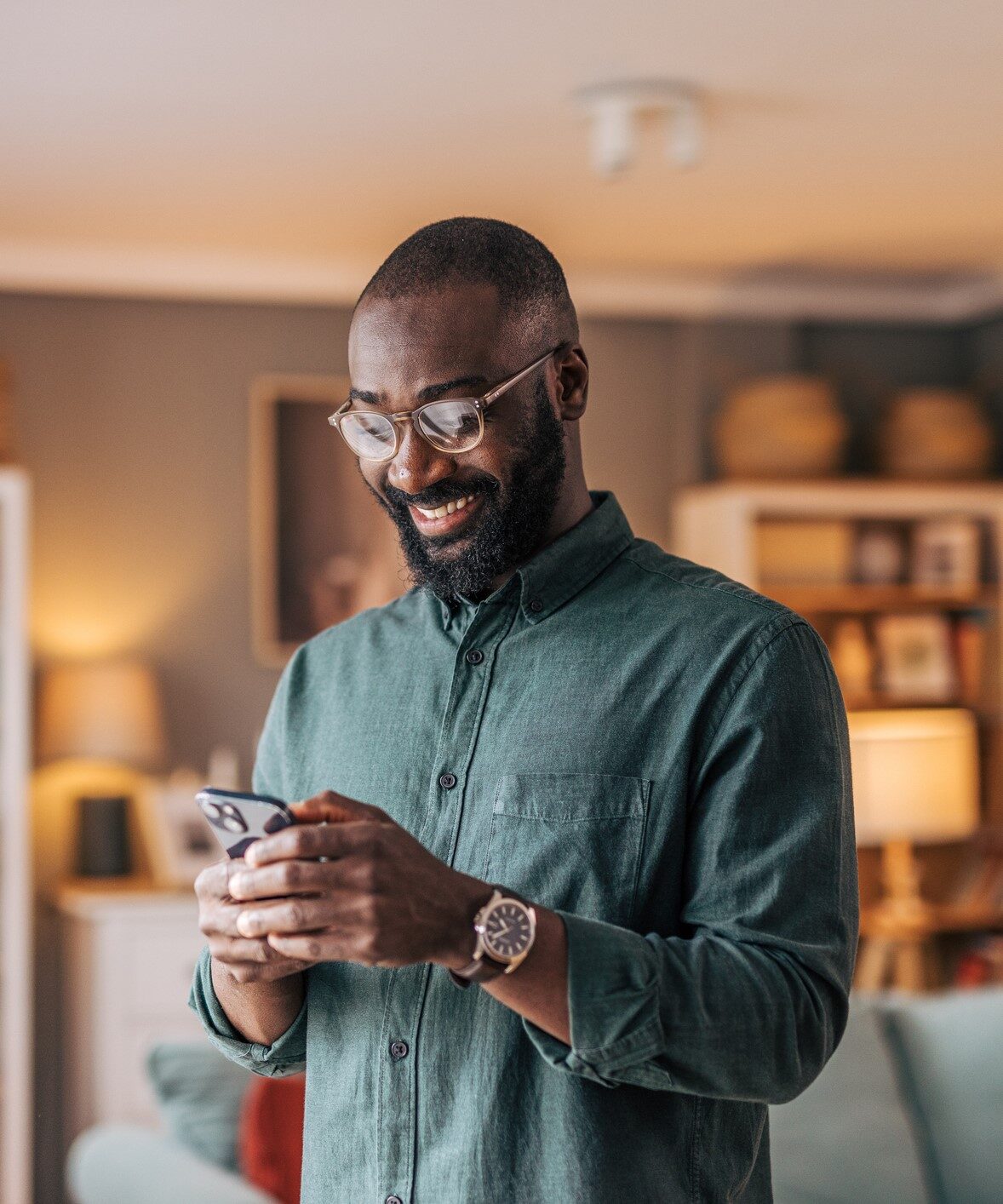 Happy man standing in his living room, smiling while using phone.