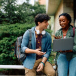 Happy African American student and her friend surfing the net on laptop at campus.