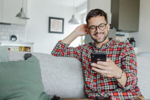 Man smiling using phone on couch.