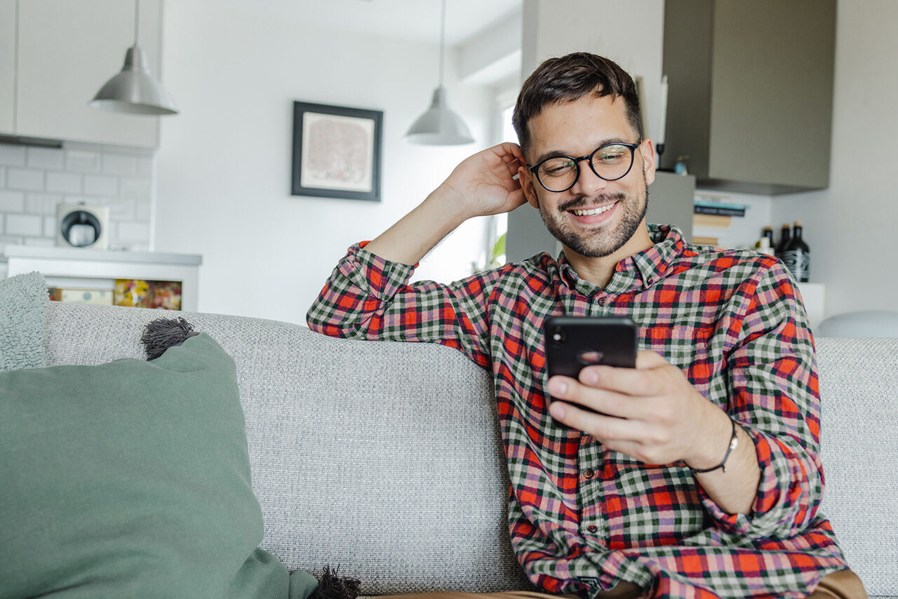 Man smiling using phone on couch.