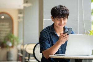 Man at coffee shop using phone and laptop