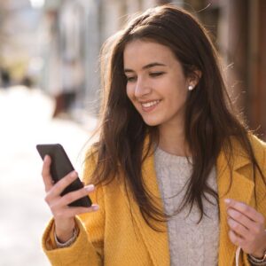 Smiling woman with shopping bag outside looking at phone.
