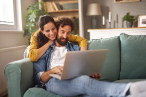 Smiling couple relaxing on sofa using laptop.