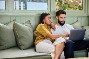 Young couple looking at their laptop at home on the couch.