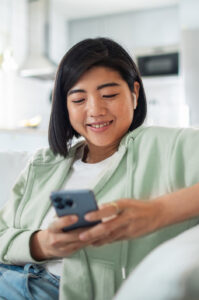 Woman smiling at home on couch using phone.