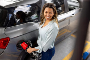 Happy Latin American woman refueling her car at a gas station and smiling