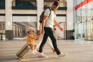 Cheerful dad with his little girl sitting on luggage at the airport.