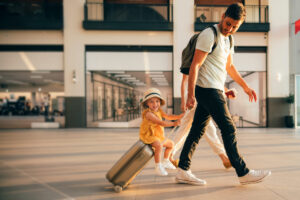 Cheerful dad with his little girl sitting on luggage at the airport.