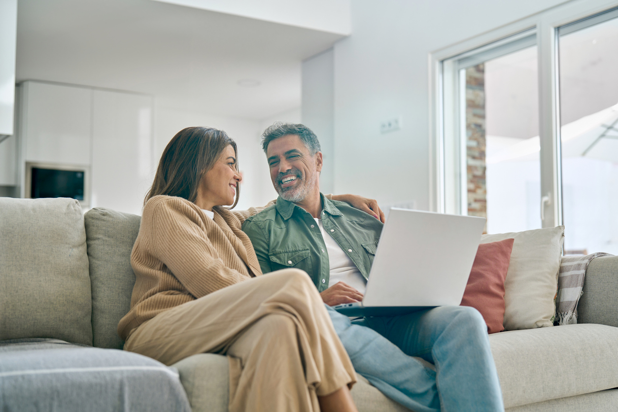 Happy mature couple using laptop relaxing on sofa in living room. Candid shot.