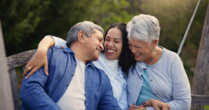 Happy family, senior parents or woman on bench in nature, hug or bonding in smile on retirement. Mature man, mother and older daughter for together in laughter, lounge and embrace for love in garden