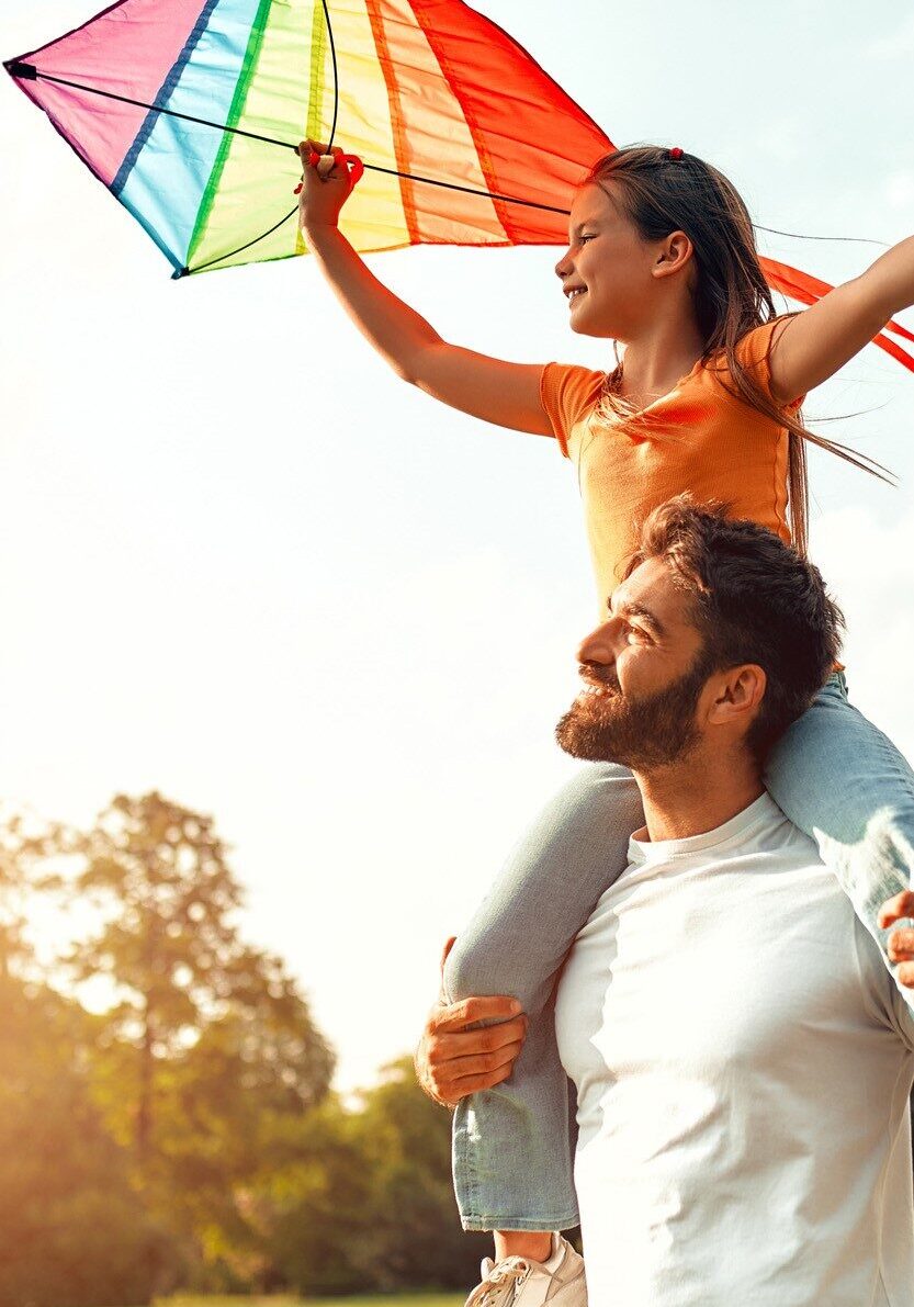 Dad with daughter on shoulders holding a kite.