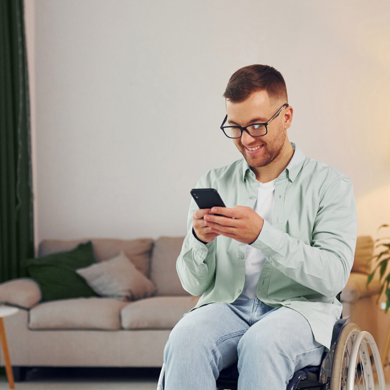 Man in wheelchair looking at his phone in his living room.