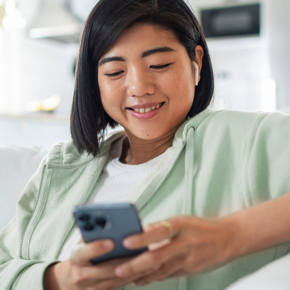 Woman smiling at home on couch using phone.
