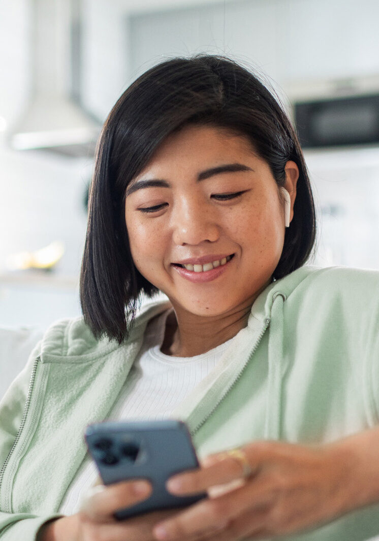 Woman smiling at home on couch using phone.