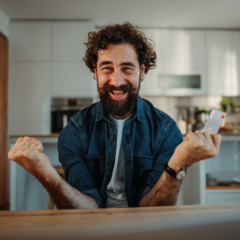Man Holding Platinum Credit Card Excitedly In Denim Shirt